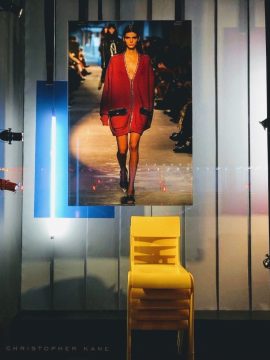 A backrop window element display by PW Shop for the Christopher Kane clothing brand. A banner, stacked chairs and neon lights.