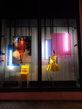 A backrop window element display by PW Shop for the Christopher Kane clothing brand. A mannequin, stacked chairs and neon lights.